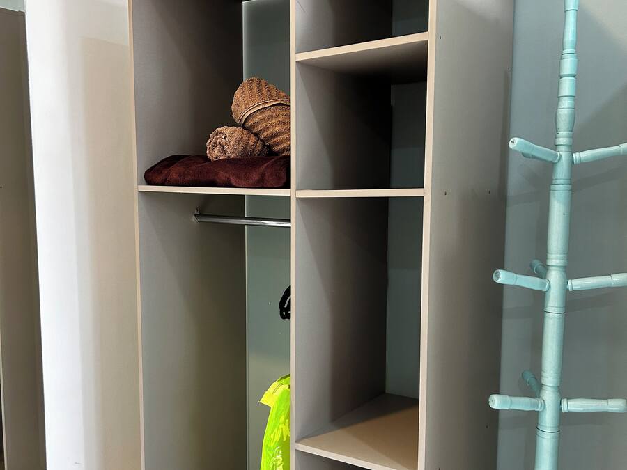 Ein grauer Kleiderschrank mit mehreren Einlegeböden und einer Kleiderstange, sowie eine blaue Leiter.