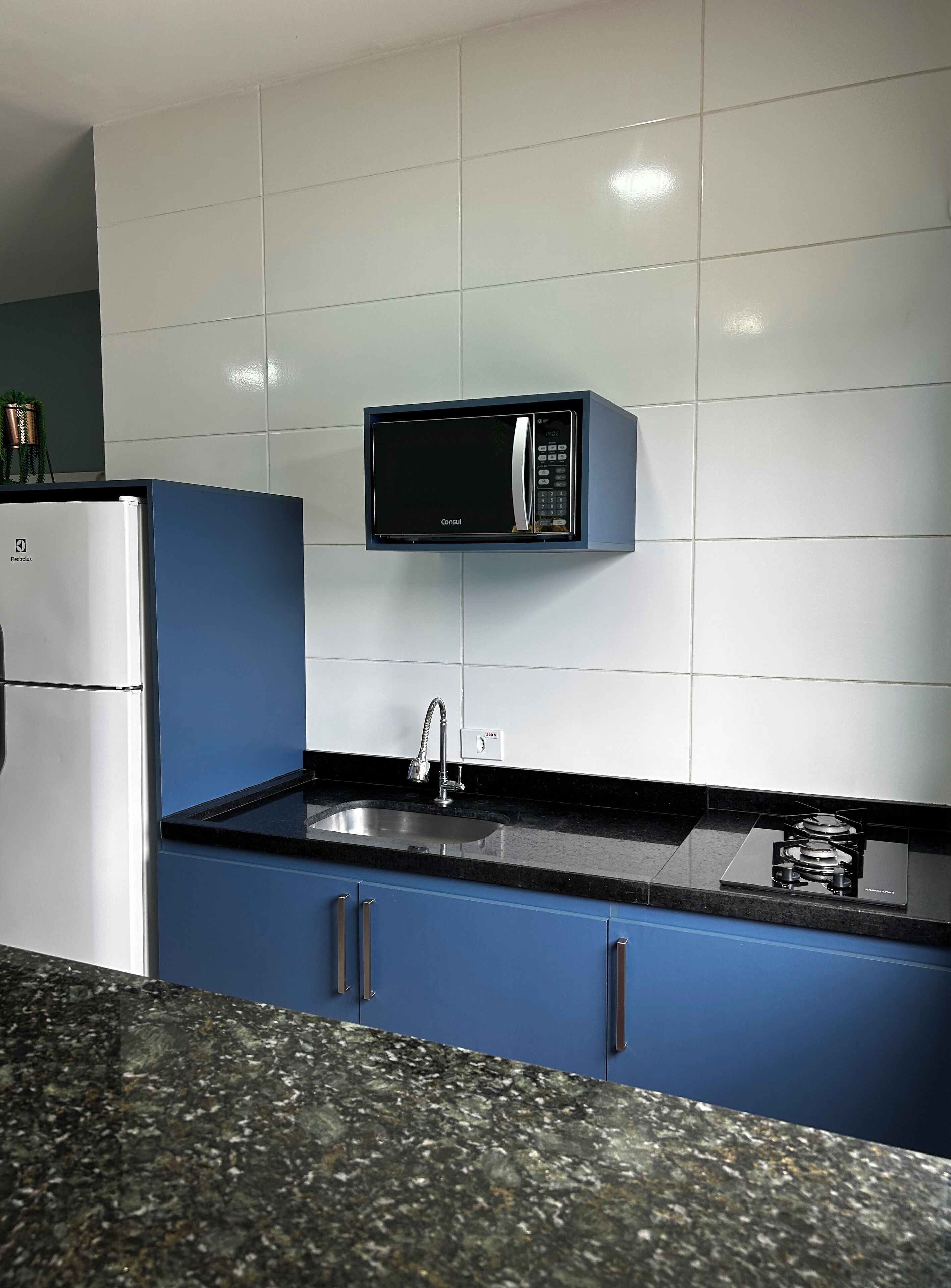 A kitchen with a built-in microwave, stainless steel refrigerator, and a granite countertop.