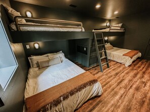 A bunk bed room with a ladder, a desk, and a window. - The Roosevelt | Modern Cabin in the Trees (Logan)