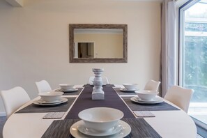 A dining table set for six with white chairs, a central decorative piece, and a large mirror on the wall. - Toast Stays - The Sunroom House (Durham)