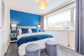A bedroom with a large bed, two bedside tables, a window with curtains, and a view of buildings outside. - Toast Stays - The Sunroom House (Durham)