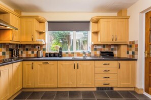 A kitchen with wooden cabinets, a black countertop, and a window with a view of greenery. - Toast Stays - The Sunroom House (Durham)