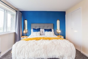 A bedroom with a large bed, two bedside lamps, a window with curtains, and a wardrobe. - Toast Stays - The Sunroom House (Durham)