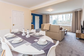A dining area with a round table set for four, a beige sofa, and a window with curtains. - Toast Stays - The Sunroom House (Durham)