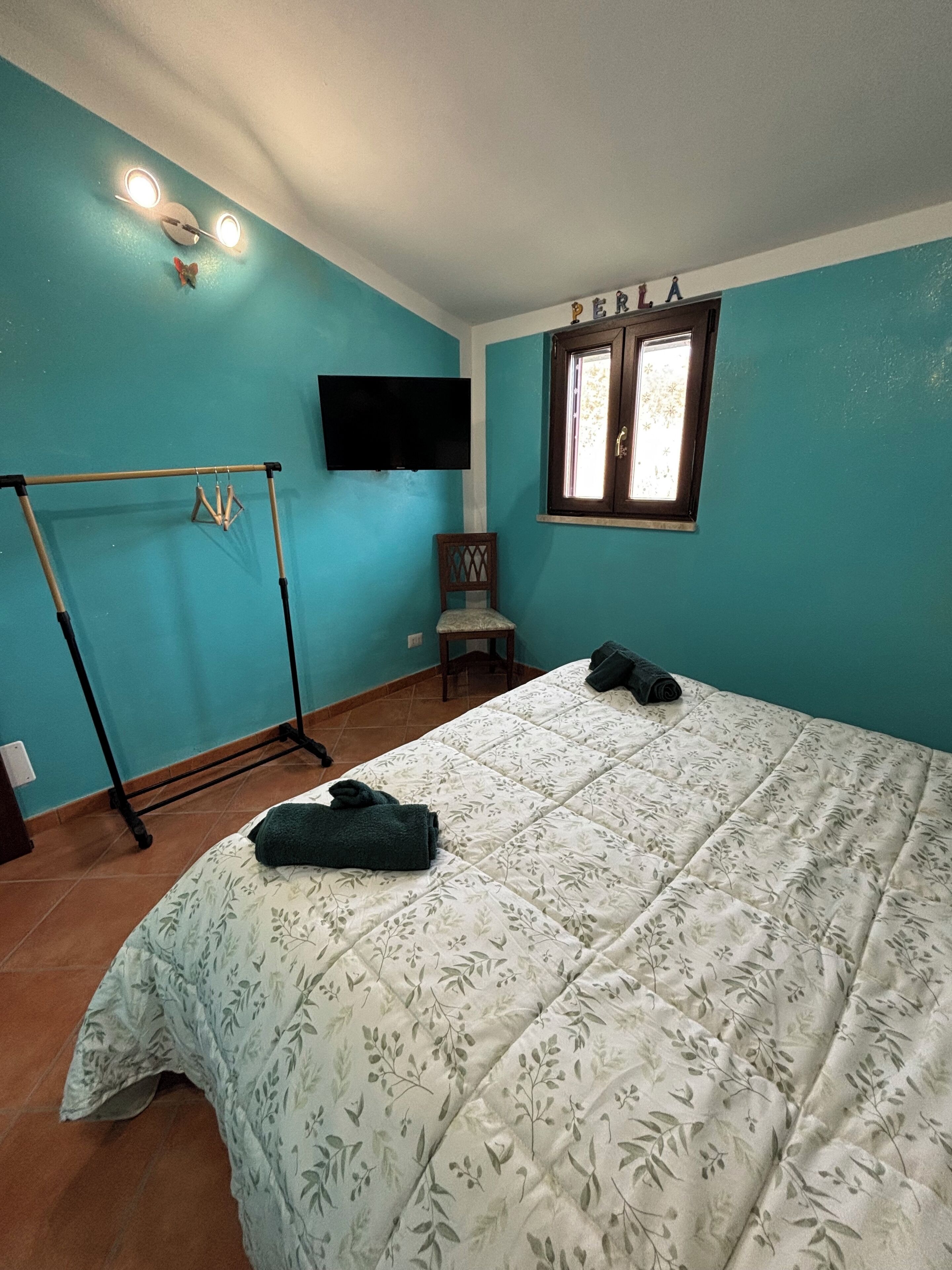 A bedroom with a bed, a TV mounted on the wall, a window, and a chair.