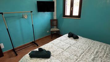 A bedroom with a bed, a TV mounted on the wall, a window, and a chair.