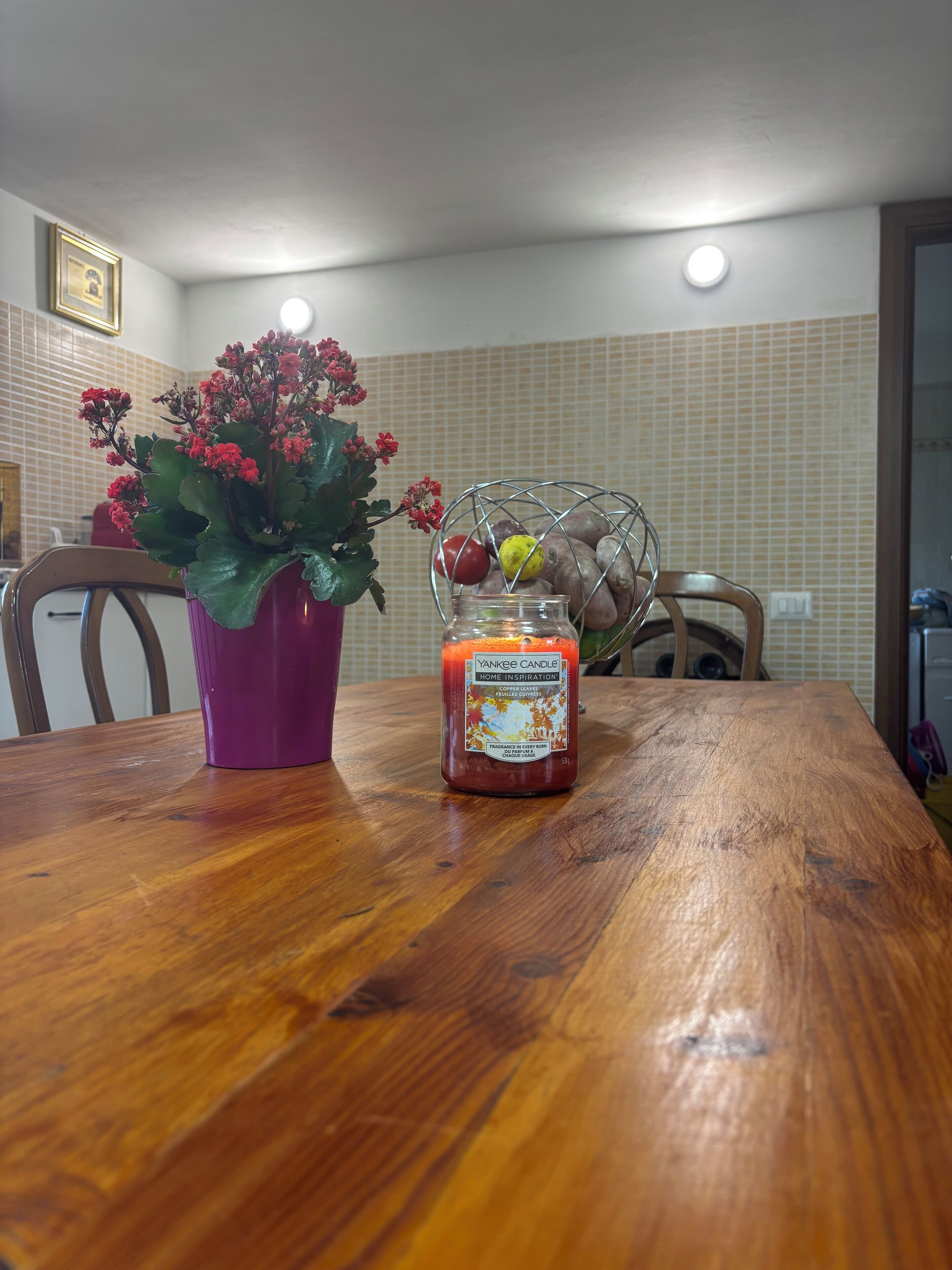 Ein Holztisch mit Kerze, einer Topfpflanze und einer Obstschale.