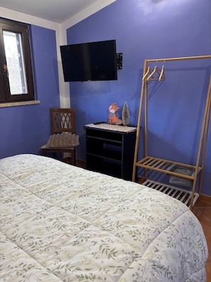 A bedroom with a bed, a TV mounted on the wall, a wooden chair, and a small table with a fox decoration. - Discover the relaxation of the mountains in this detached villa surrounded by greenery. (Abruzzo)