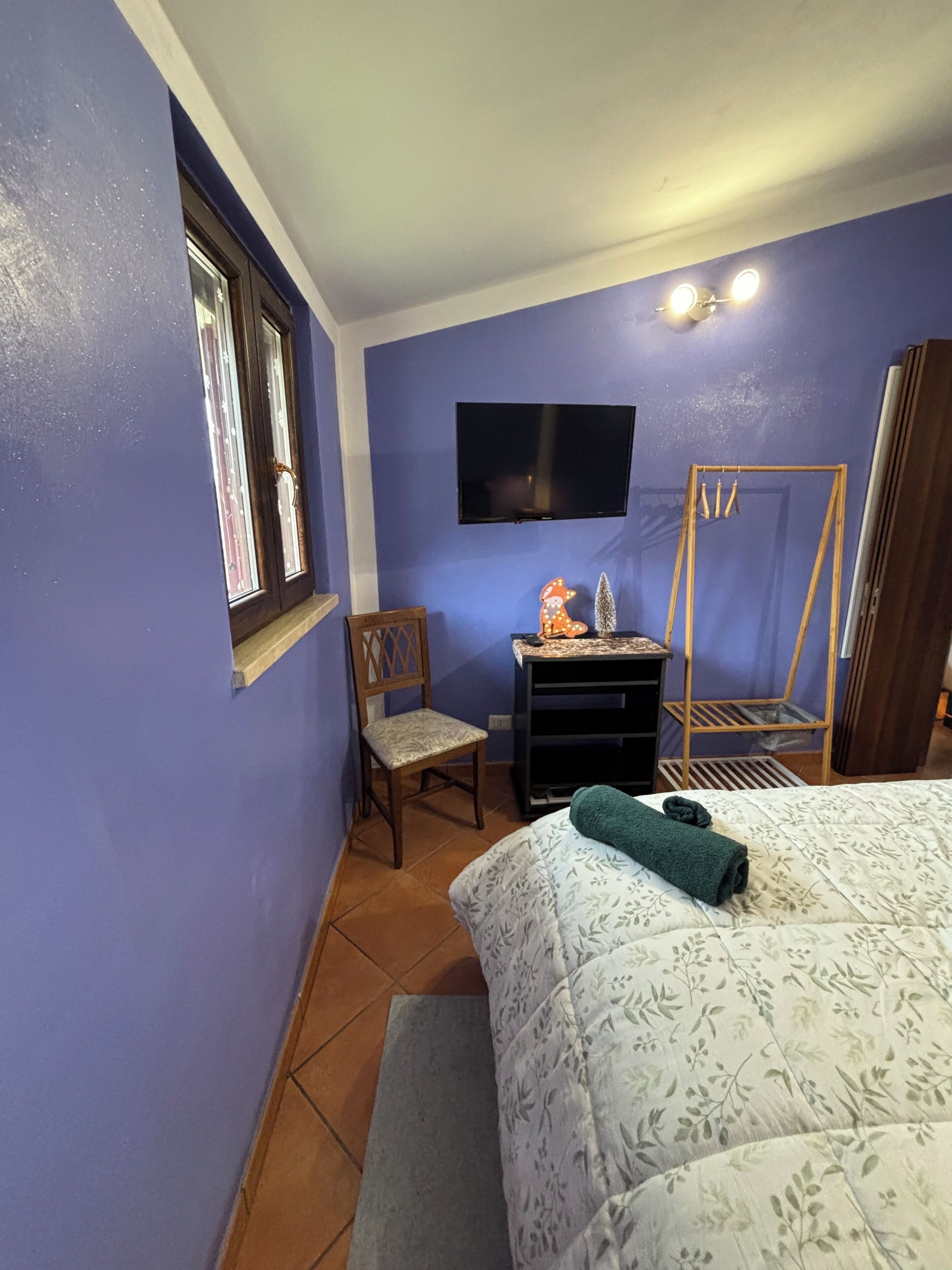Une chambre à coucher avec un lit, une chaise, un bureau, une télévision et une fenêtre.