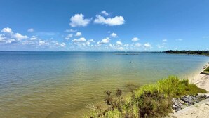 A clear view of a calm lake with a sandy beach and some vegetation in the foreground. - Pelican's Perch: Kayaks, Views & More! (Escambia County)