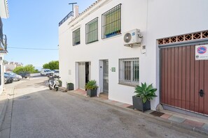 Un bâtiment blanc avec une porte de garage marron, un scooter garé et des plantes en pot.