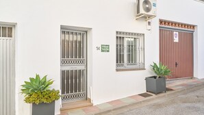 Un bâtiment à la façade blanche, portant le numéro 14, avec une porte rouge, des fenêtres grillagées et deux plantes en pot.