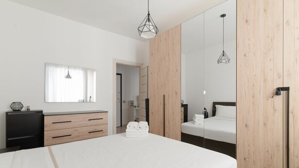 A modern bedroom with a large bed, a dresser, a mirror, and a wardrobe. - GuestHost - Cute Apartment Navigli Milano (Milan)