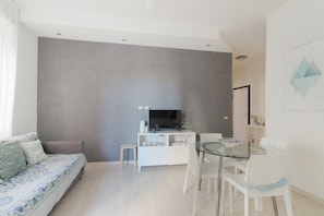 Un salon moderne avec un canapé, une table à manger en verre et un téléviseur posé sur un meuble blanc.