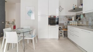 A modern kitchen with white cabinetry, a glass dining table, and a stainless steel oven. - GuestHost - Cute Apartment Navigli Milano (Milan)