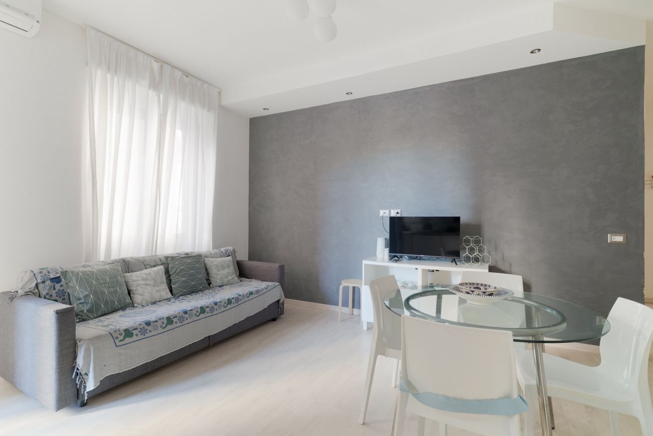 A modern living room with a sofa, a glass table, and a flat-screen TV.