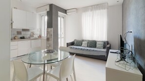 A modern kitchen with white cabinets, a glass dining table, and a gray sofa with patterned cushions. - GuestHost - Cute Apartment Navigli Milano (Milan)