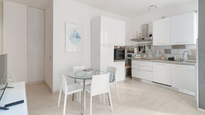 A modern kitchen with white cabinets, a dining table with chairs, and a kitchen island. - GuestHost - Cute Apartment Navigli Milano (Milan)