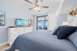 A bedroom with a bed, a ceiling fan, a TV, a dresser, and a view of the outdoors. - Sunrise Serenity Summer House 1101A (Orange Beach)