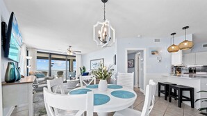 A modern kitchen with white cabinetry, a dining area with a round table and white chairs, and a large window offering a view of the ocean. - Sunrise Serenity Summer House 1101A (Orange Beach)