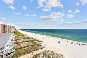 A beach with a wooden boardwalk, a hotel with balconies, and a clear blue sky. - Sunrise Serenity Summer House 1101A (Orange Beach)