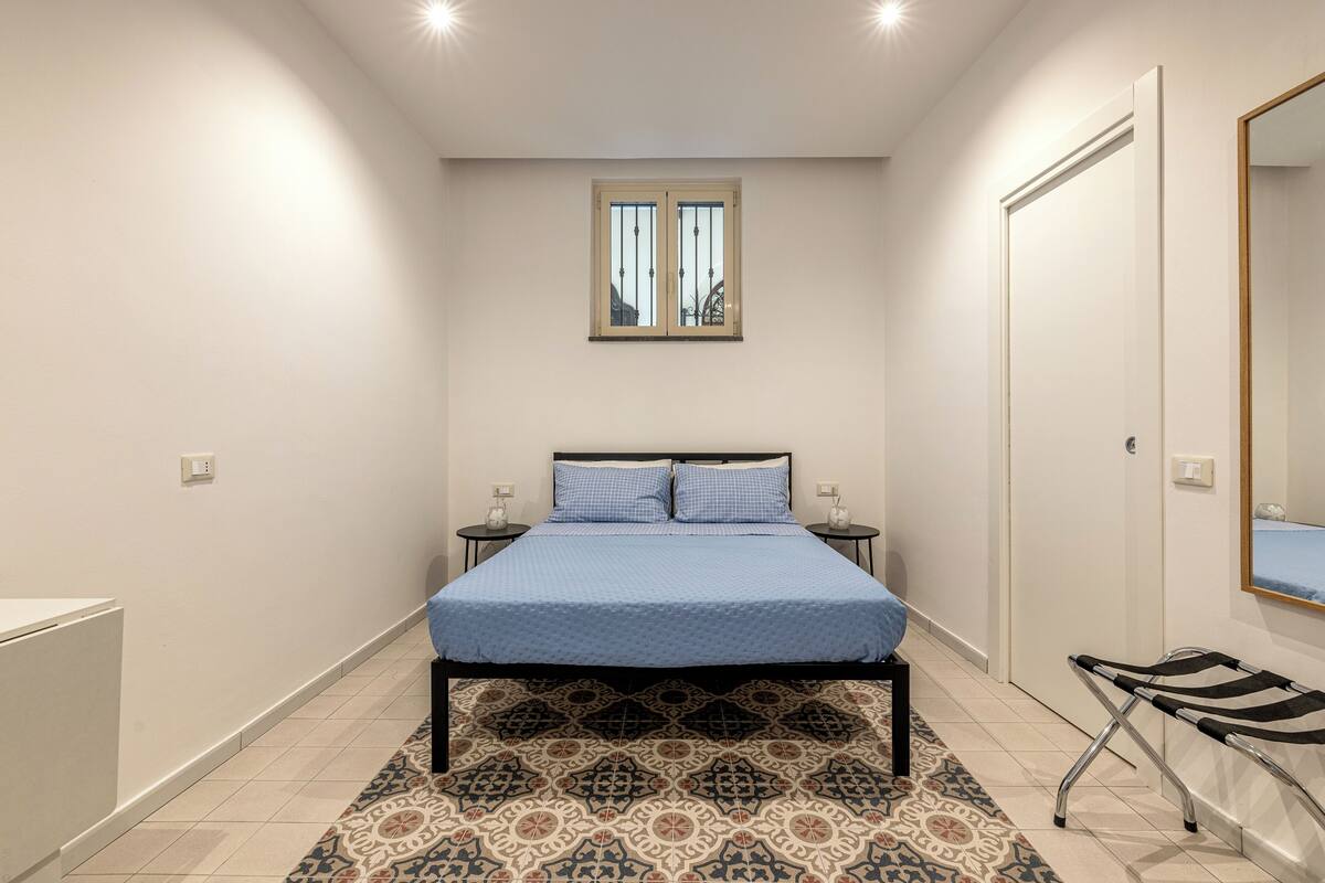 A bedroom with a bed, bedside tables, a window, a patterned rug, and a chair.