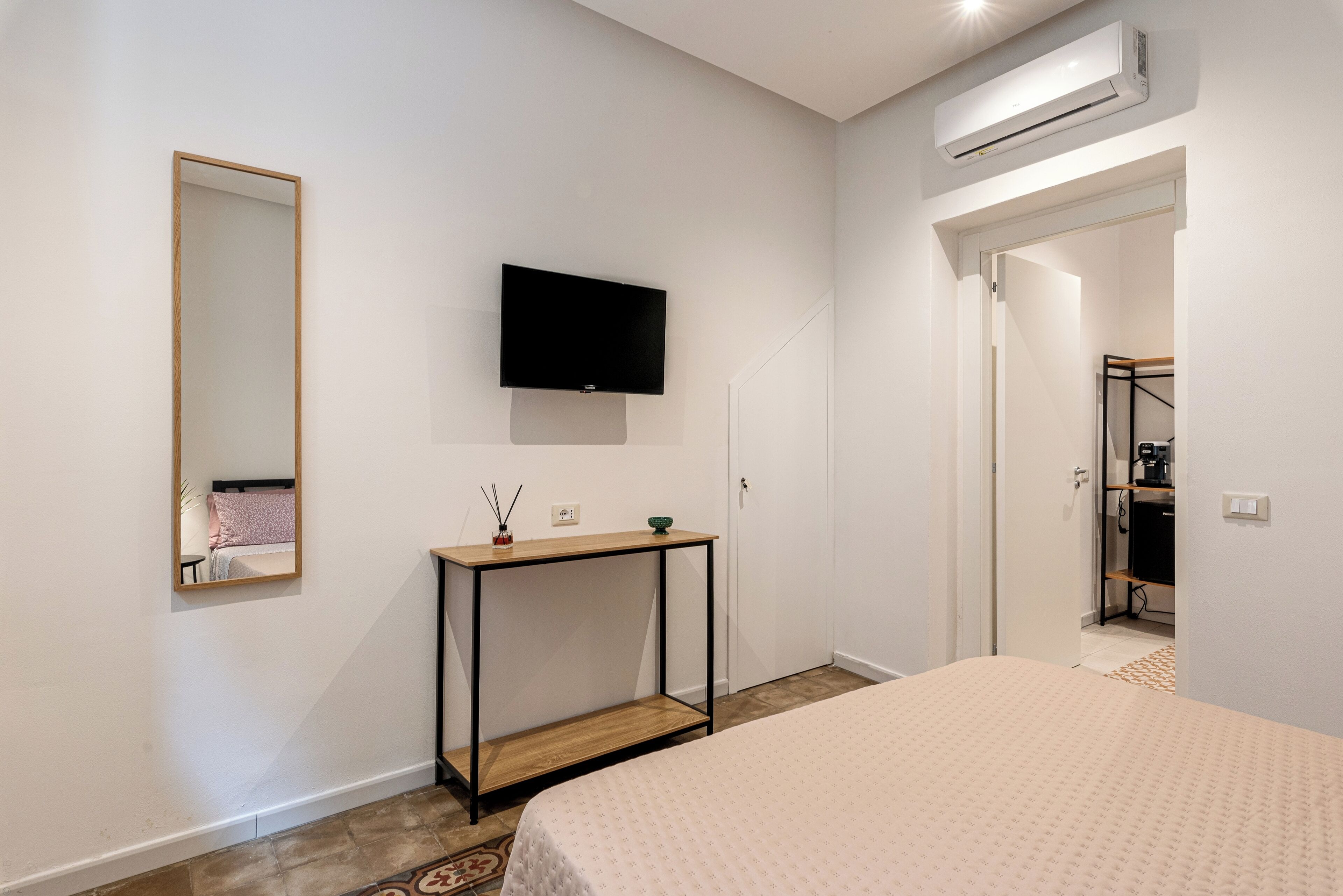 Ein Schlafzimmer mit einem Bett, einem an der Wand montierten Fernseher, einem Nachttisch mit Lampe und einem Kleiderschrank.