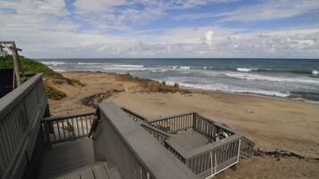 Une terrasse en bois donnant accès à une plage avec vue sur l’océan.