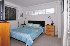 A bedroom with a bed, a wooden dresser, a nightstand, a desk, and a window with blinds. - Stuart Beach House- Ocean-to-river with stunning views, private dock & hot tub! (Stuart)