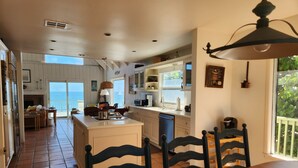 A spacious kitchen with a large island, white cabinetry, and a view to the outside. - Stuart Beach House- Ocean-to-river with stunning views, private dock & hot tub! (Stuart)