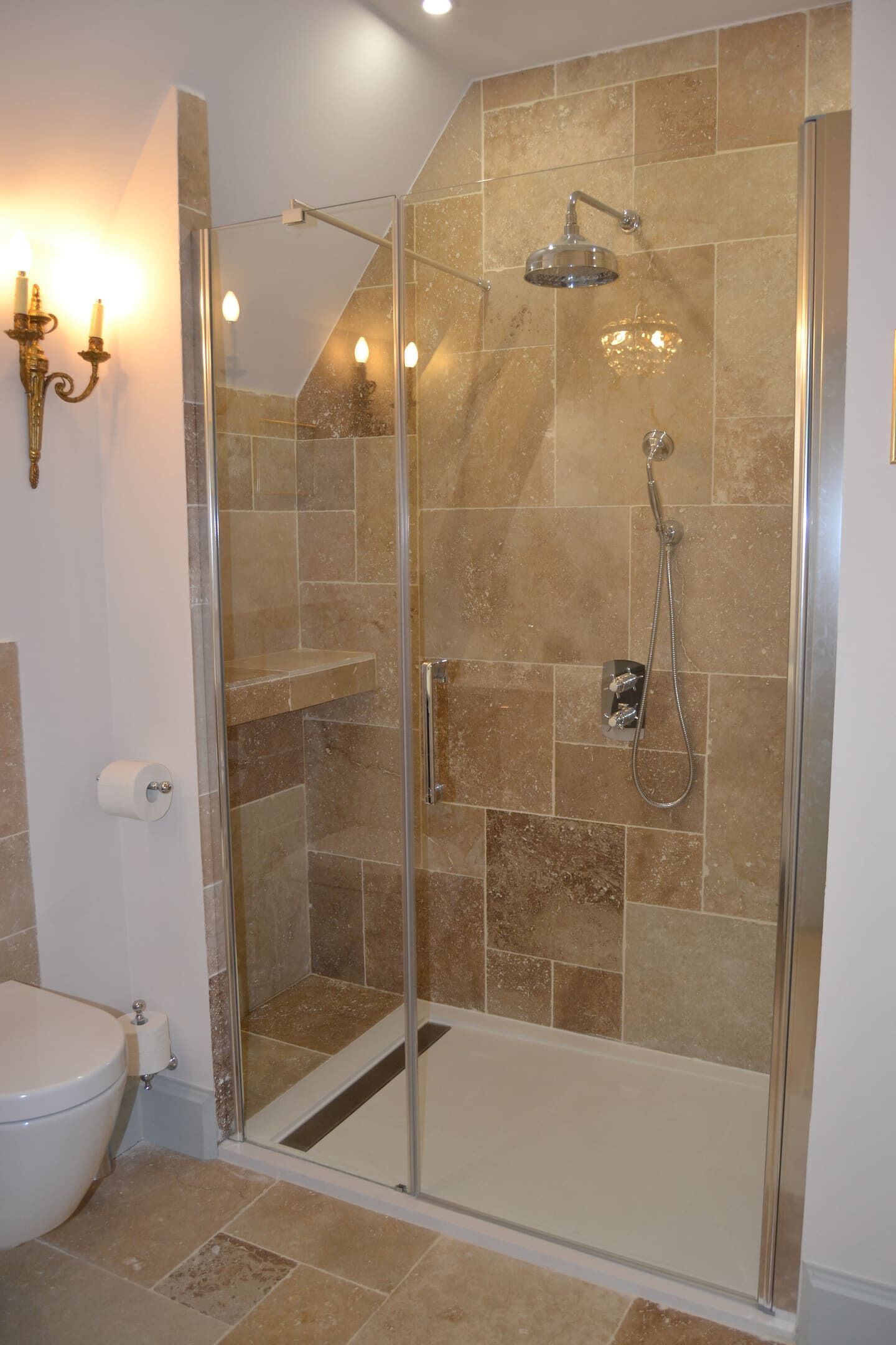 Un baño moderno con ducha envuelta en vidrio, azulejos color beige y un inodoro.