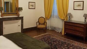 A bedroom with a bed, a dresser, a chair, a chandelier, and a large mirror.