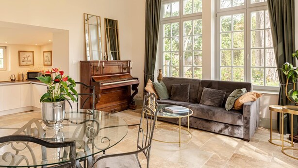 A living room with a piano, a glass table, a sofa, and large windows with curtains. - Château St Justin (Saint-Justin)