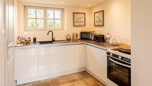A modern kitchen with white cabinets, a sink, a microwave, a coffee maker, and a stove. There are two framed pictures on the wall and a window above the sink. - Château St Justin (Saint-Justin)