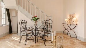 A dining area with a table and chairs, a vase with flowers, a staircase, and a wall-mounted table with lamps. - Château St Justin (Saint-Justin)