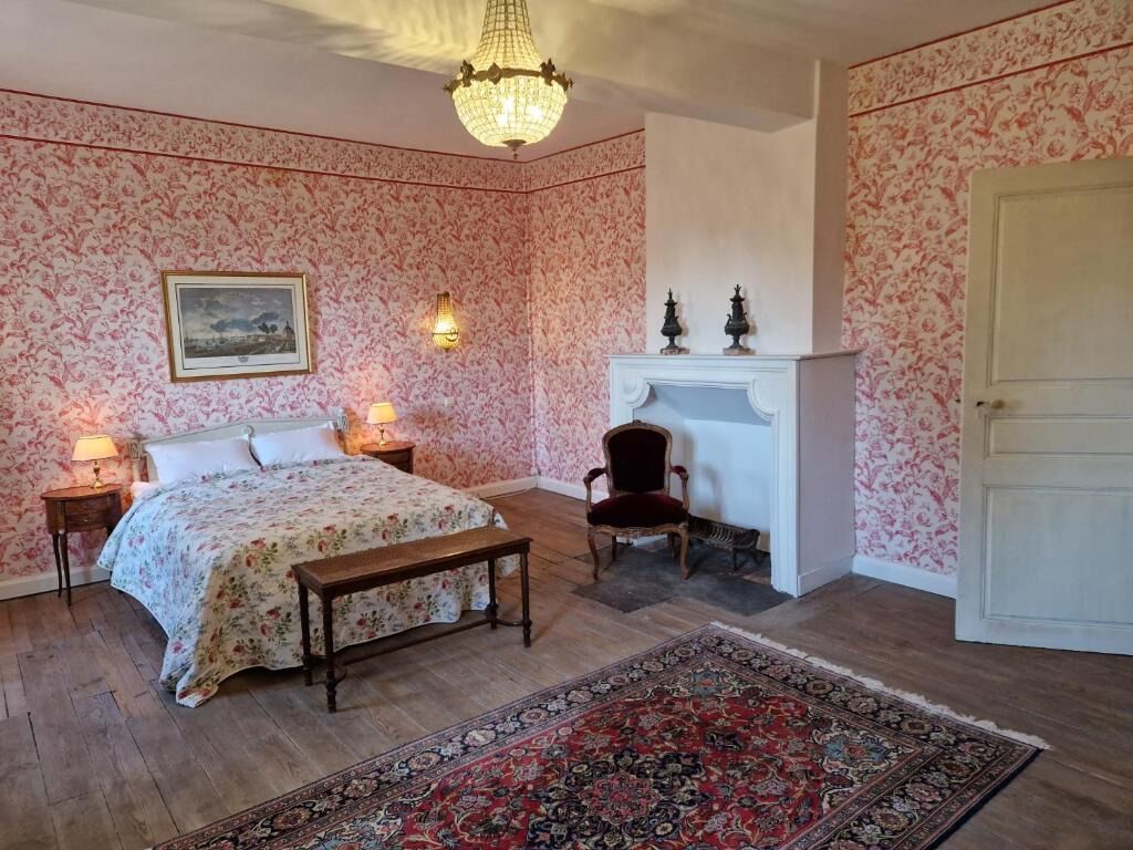 A bedroom with a bed, bedside lamps, a chair, a fireplace, and a rug.