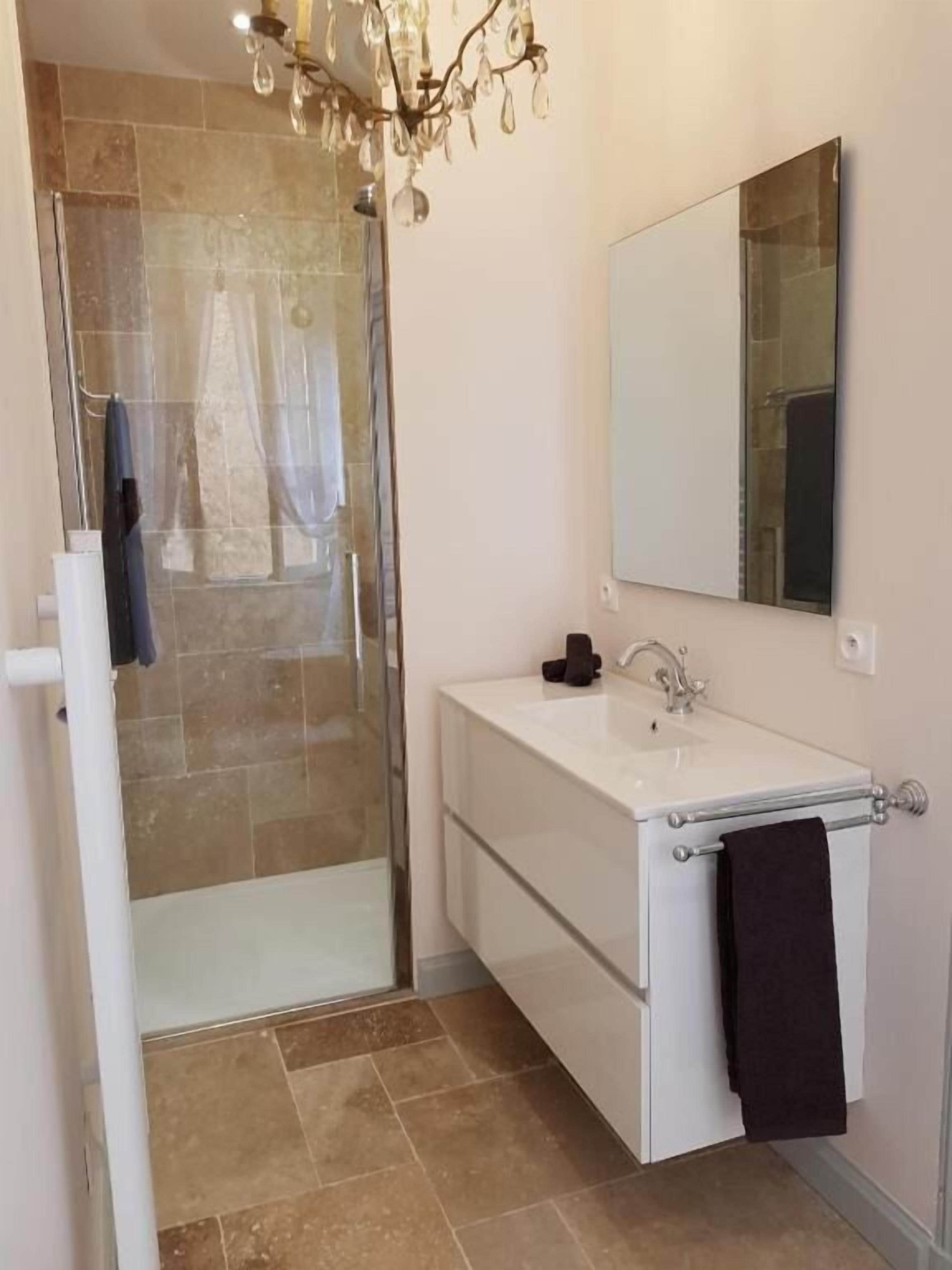 A bathroom with a glass shower enclosure, a white sink with a black towel, and a mirror above the sink.