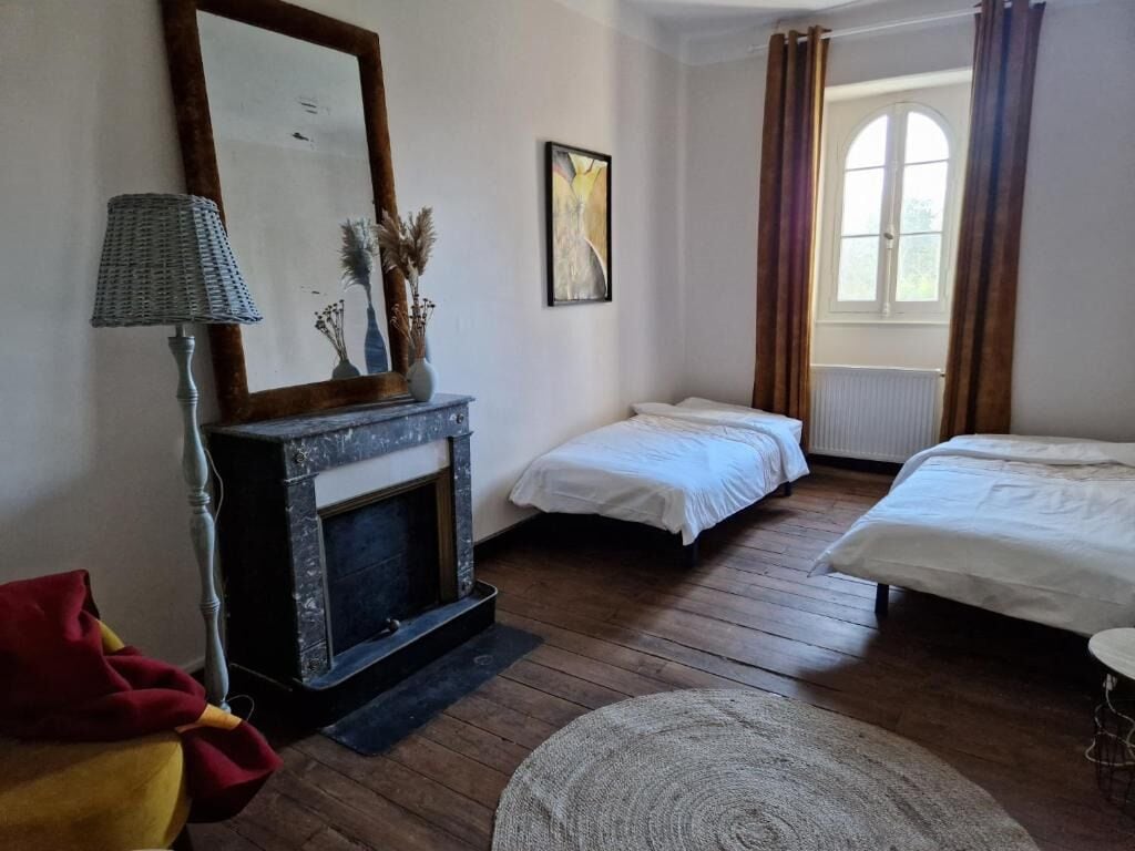 Een slaapkamer met twee eenpersoonsbedden, een open haard, een lamp en een raam met gordijnen.
