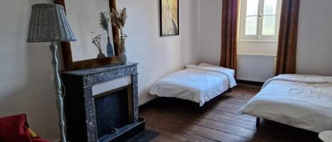 A bedroom with two single beds, a fireplace, a lamp, and a window with curtains.