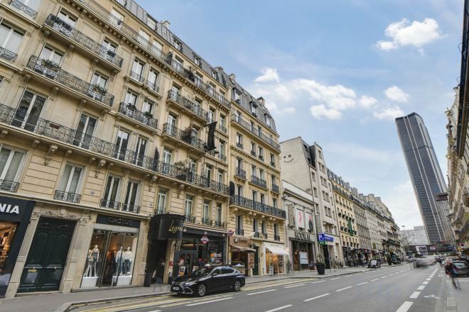 Une rue bordée d’immeubles à plusieurs étages, un ciel dégagé et une voiture garée.