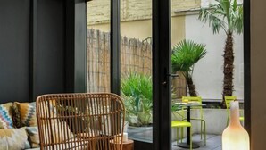 Un'accogliente zona con seduta in vimini e cuscini, un tavolino con candele e vista su un patio con piante e sedie.
