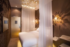 A hotel room with a bed, a bathroom with a sink and mirror, and a wall-mounted light fixture. - Legend Hôtel Paris (Paris)