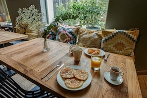 A wooden dining table with breakfast items, including pancakes, coffee, and orange juice. - Legend Hôtel Paris (Paris)