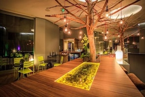 A restaurant with a wooden table, chairs, hanging lights, and a tree-like structure. - Legend Hôtel Paris (Paris)
