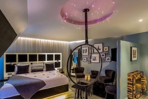 A modern bedroom with a circular ceiling light, a bed with a headboard, and a seating area with chairs. - Legend Hôtel Paris (Paris)