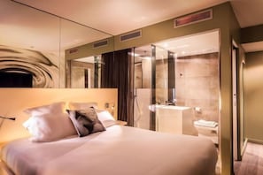 A hotel room with a large bed, a bedside table, a mirror, a shower area, and a toilet. - Legend Hôtel Paris (Paris)
