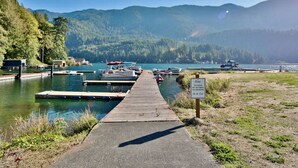 A dock leading to a lake with boats, surrounded by forested hills. - Cornerstone Haven – A Family Lakeside Escape (Port Angeles)