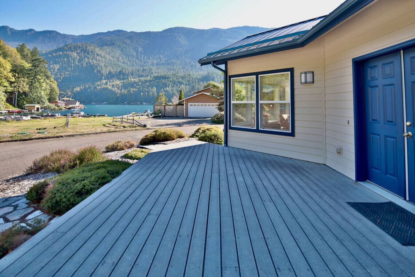 Una casa con terraza de madera, puerta azul y vista a las montañas y un lago.