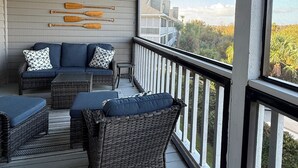 En inglasad veranda med möbler i rotting, en takfläkt och utsikt över ett hus och träd.