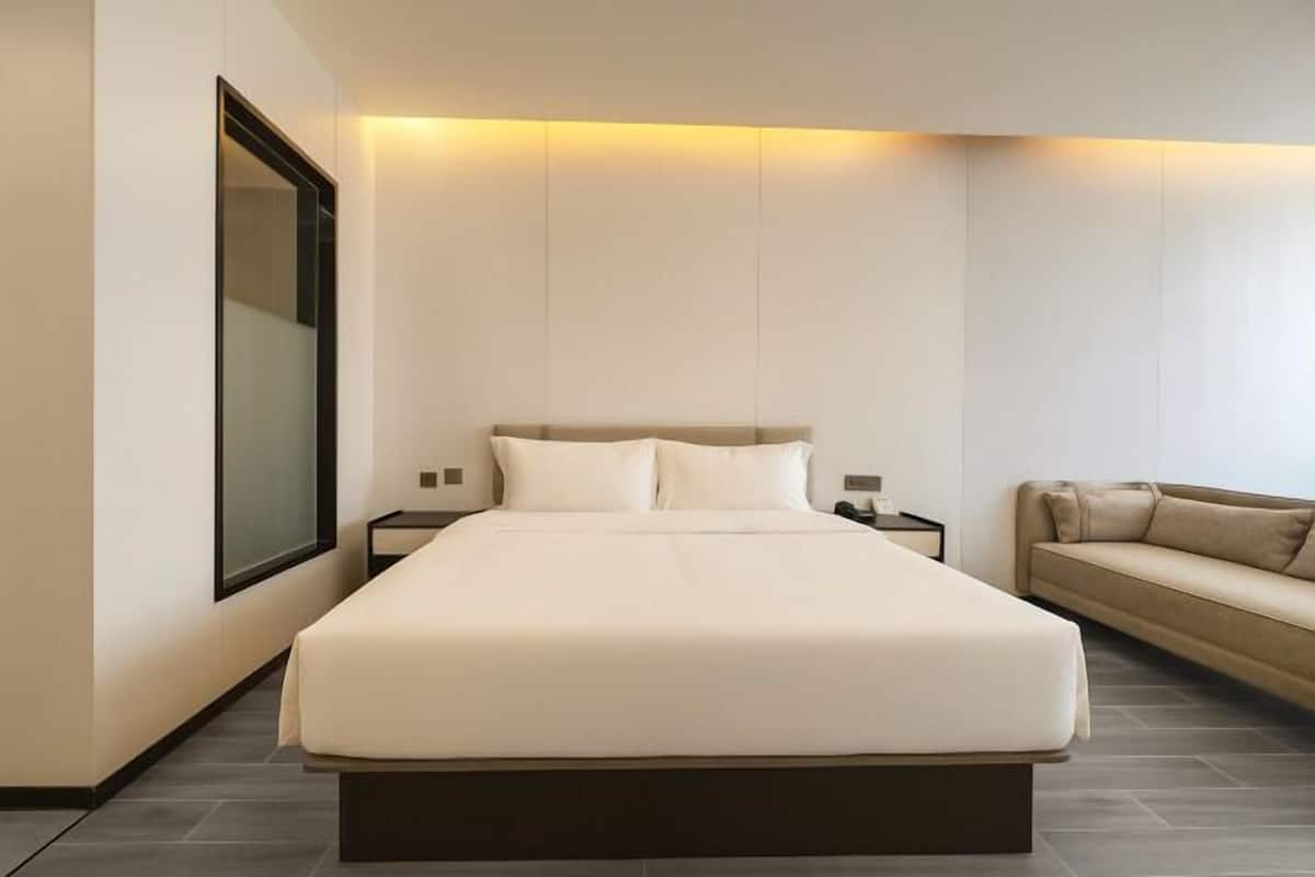 Une chambre d’hôtel moderne avec un grand lit, une table de chevet, un canapé et un grand miroir.